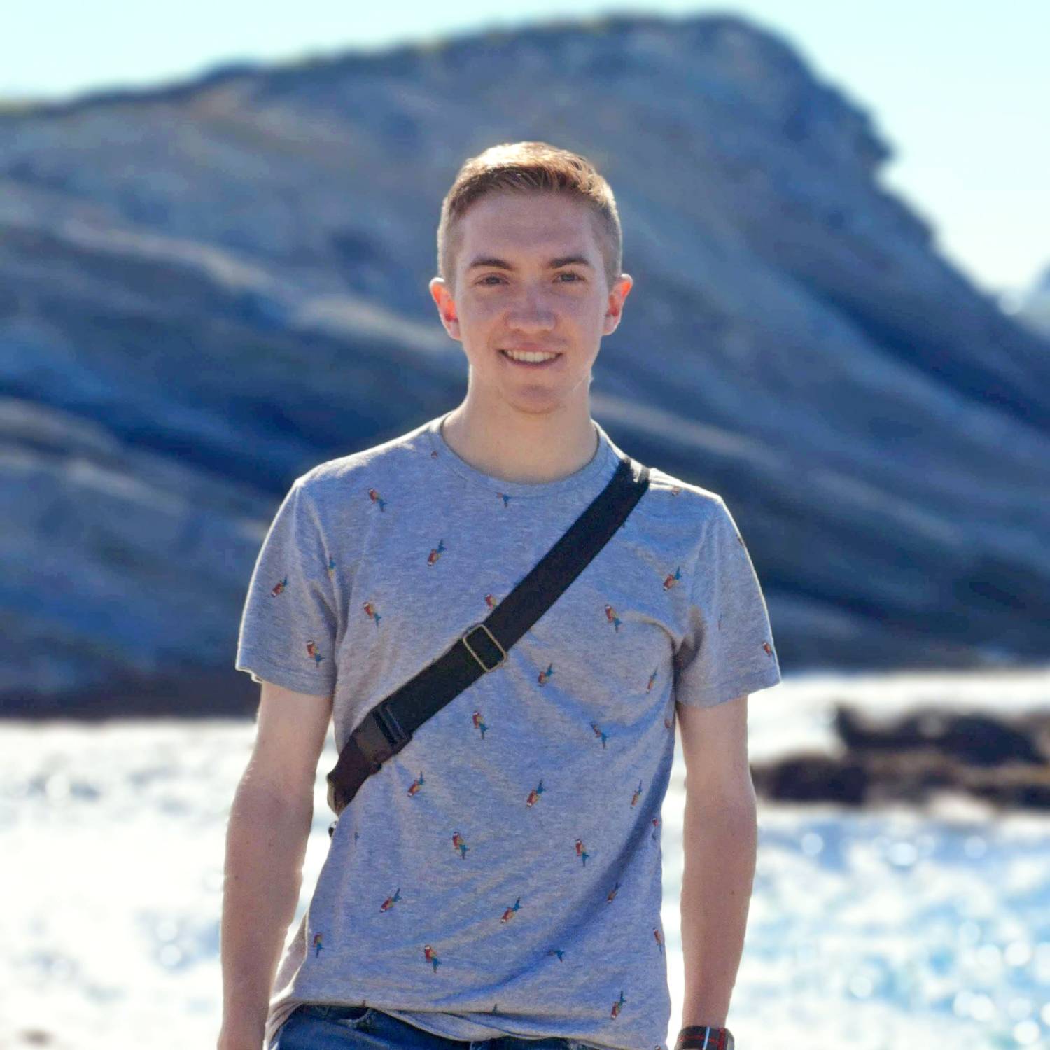 Smiling person in a gray t-shirt with a rocky coastal background